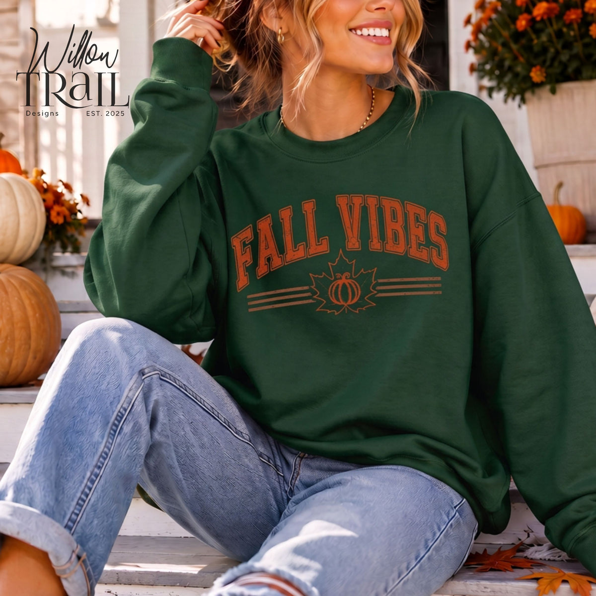 Model wearing a dark green Fall Vibes crewneck sweatshirt with orange lettering and a pumpkin design, seated on a porch.